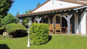 Ein Gebäude mit überdachter Terrasse, Sitzgelegenheiten im Freien und einem gepflegten Garten.
