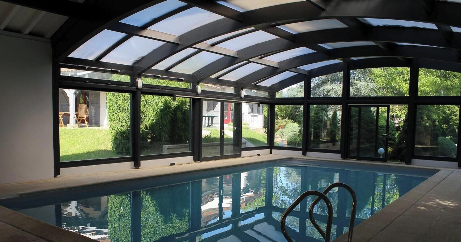 Une piscine intérieure dotée d’un toit en verre et de grandes fenêtres.