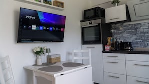 Et moderne køkken med et fladskærms-tv hængt over et hvidt spisebord, samt en mikroovn, ovn og kaffemaskine.