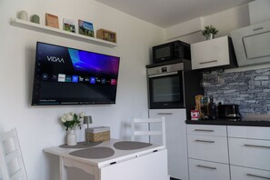 A modern kitchen with a flat-screen TV mounted above a white dining table, a microwave, oven, and a coffee machine. - Haus am Krähenbach -Sorpe
Cozy apartment with terrace & Wi-Fi near Lake Sorpe (Sundern (Sauerland))