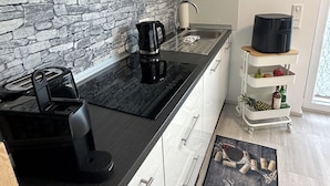 Et moderne køkken med en bagplade i sten, en kaffemaskine og en lille tralle med frugt og flasker.