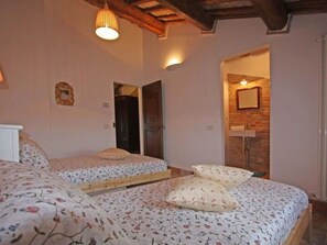 Een slaapkamer met twee eenpersoonsbedden, een houten plafond en een bakstenen muur.