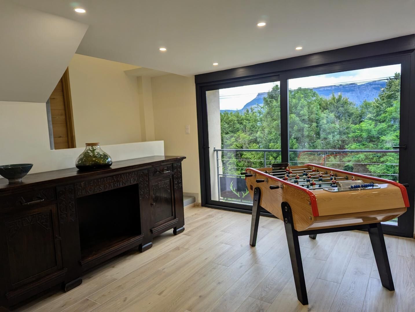 Una habitació amb una taula de futbolí, un armari de fusta fosca i una finestra gran que donava a vegetació.