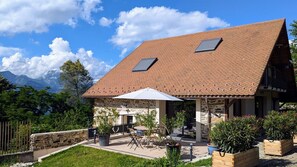 A house with a sloped roof, stone walls, a patio with outdoor furniture, and a view of mountains. - From Combeloup - MURIANETTE (MURIANETTE)