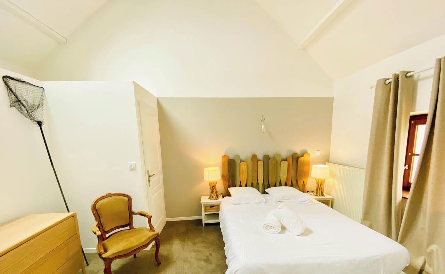 A hotel room with a bed, a chair, a desk, and a lamp.