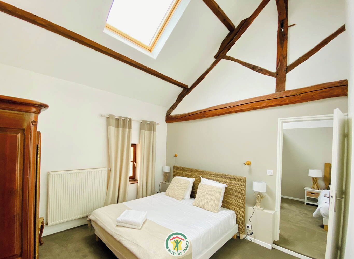 A bedroom with a bed, wooden beams, a radiator, and a window.