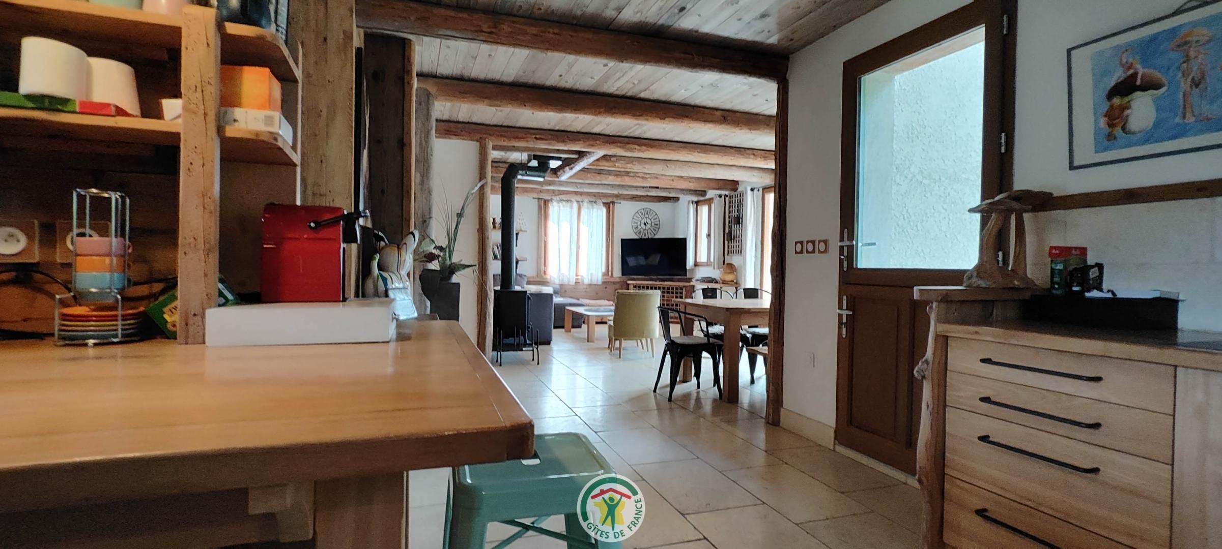 Une cuisine avec des meubles en bois, un coin repas avec une table et des chaises, et un salon avec un canapé et un téléviseur.