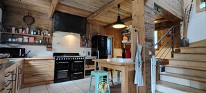 A kitchen with wooden beams, a stove, a microwave, and a refrigerator. - Clémence's Farm 5***** (VILLARD DE LANS)