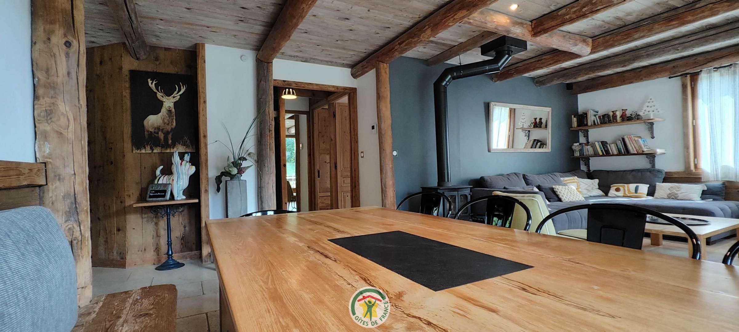 A rustic interior with exposed wooden beams, a wooden dining table, a sofa, and a bookshelf.