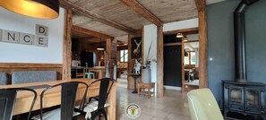 A rustic interior with a wooden dining table, chairs, a sofa, a fireplace, and a kitchen area. - Clémence's Farm 5***** (VILLARD DE LANS)