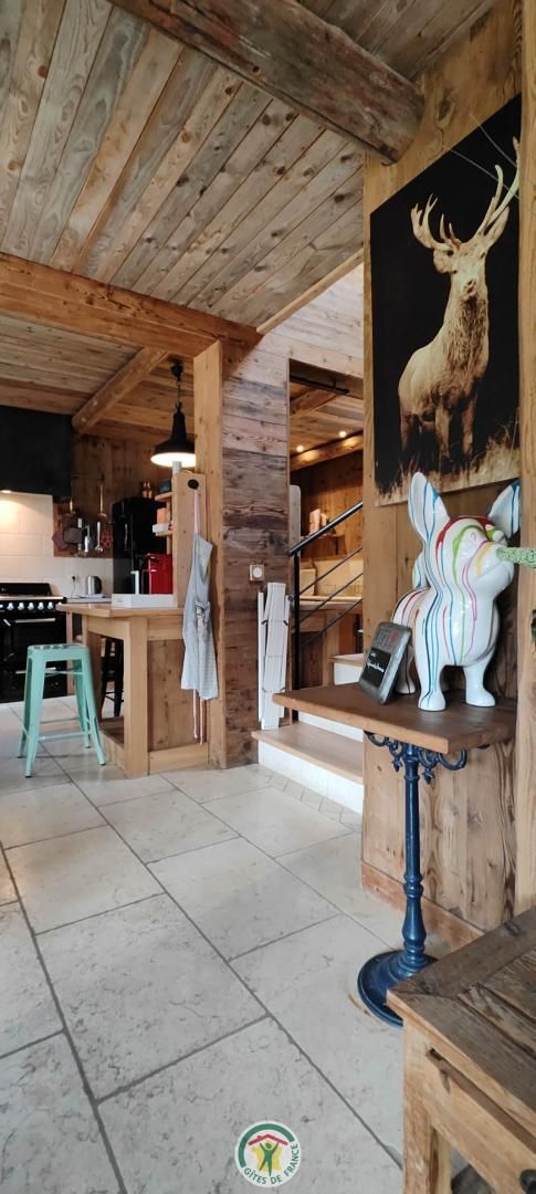A rustic interior with wooden beams, a dining area with a table and chairs, and a mounted deer head on the wall.