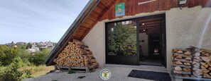 A building with a sloped roof, a stack of firewood on the ground, and a logo for 'Gites de France' on the wall. - Clémence's Farm 5***** (VILLARD DE LANS)