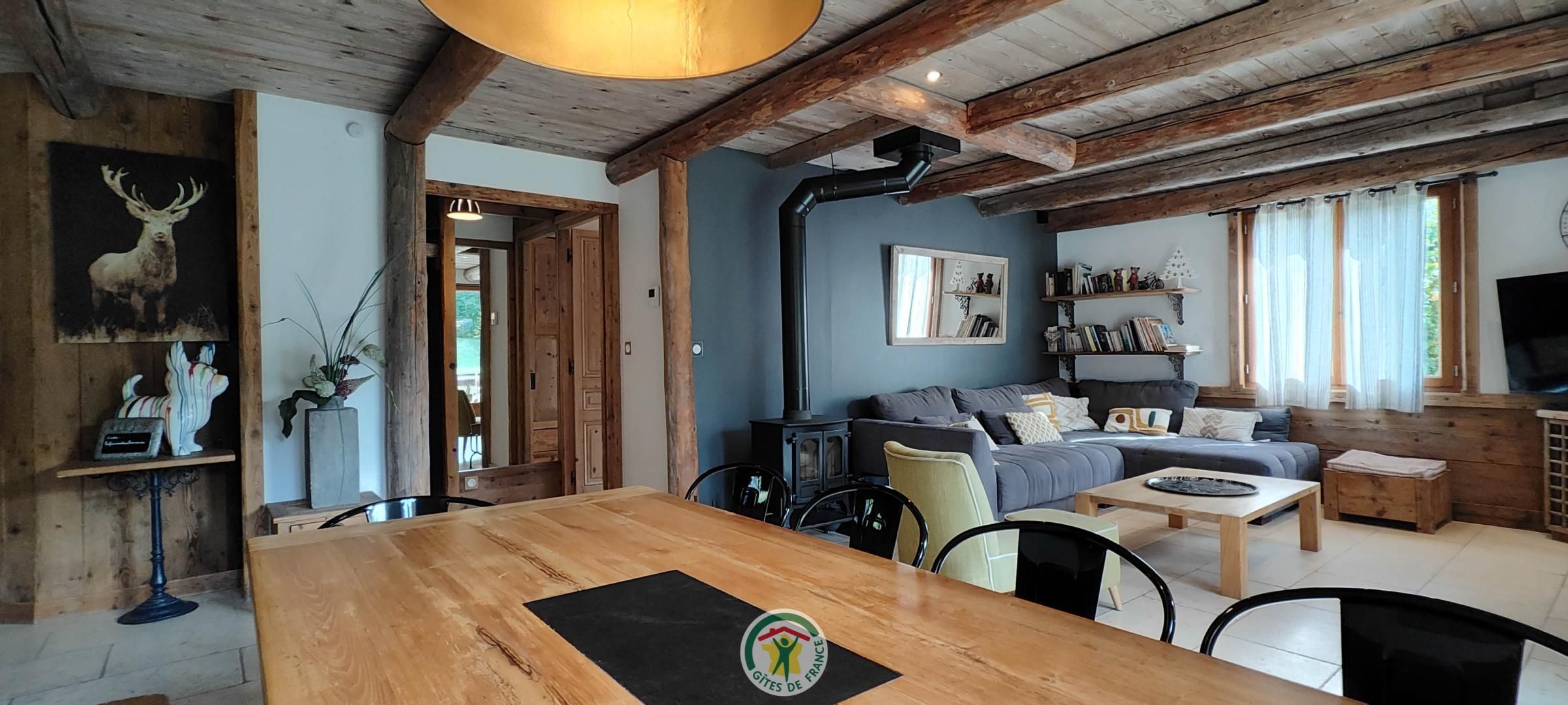 Un interior rústico con vigas de madera a la vista, una zona de comedor con mesa de madera, un sofá y una estantería.