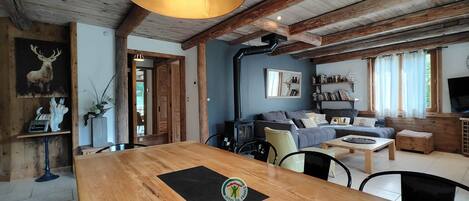 Un interior rústico con vigas de madera a la vista, una zona de comedor con mesa de madera, un sofá y una estantería.