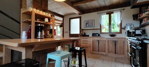 A kitchen with wooden cabinets, a coffee machine, and a window with curtains. - Clémence's Farm 5***** (VILLARD DE LANS)