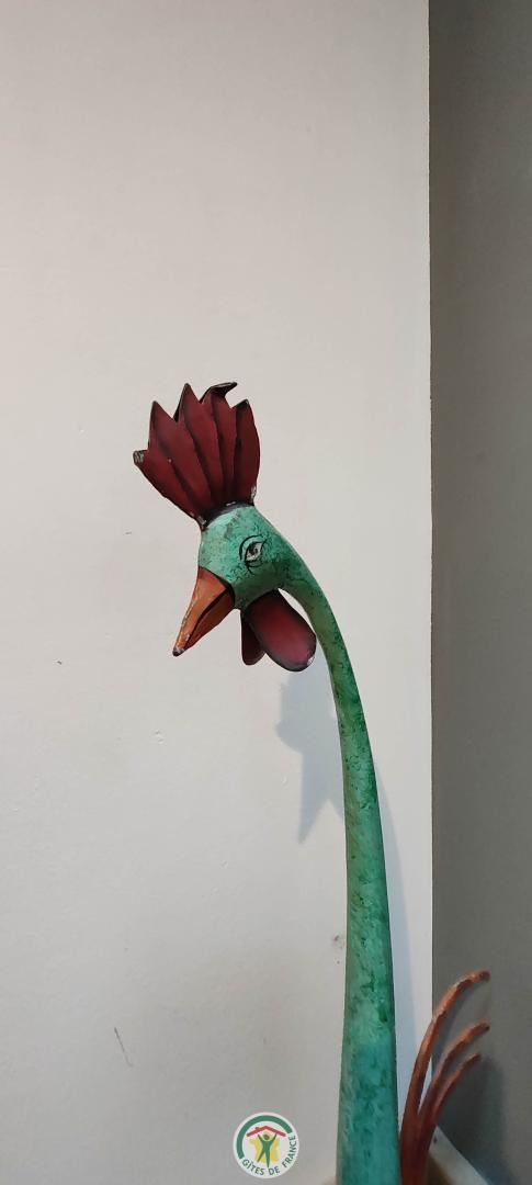 Un coq décoratif en métal, doté d’un long cou courbé et d’une crête rouge.