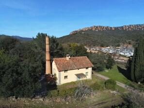 Una casa rural amb una xemeneia, envoltada d'arbres i una muntanya al fons.