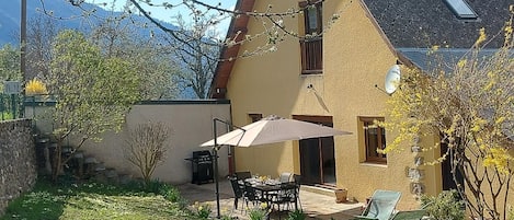 A house with a patio, a table with chairs, and a grill.