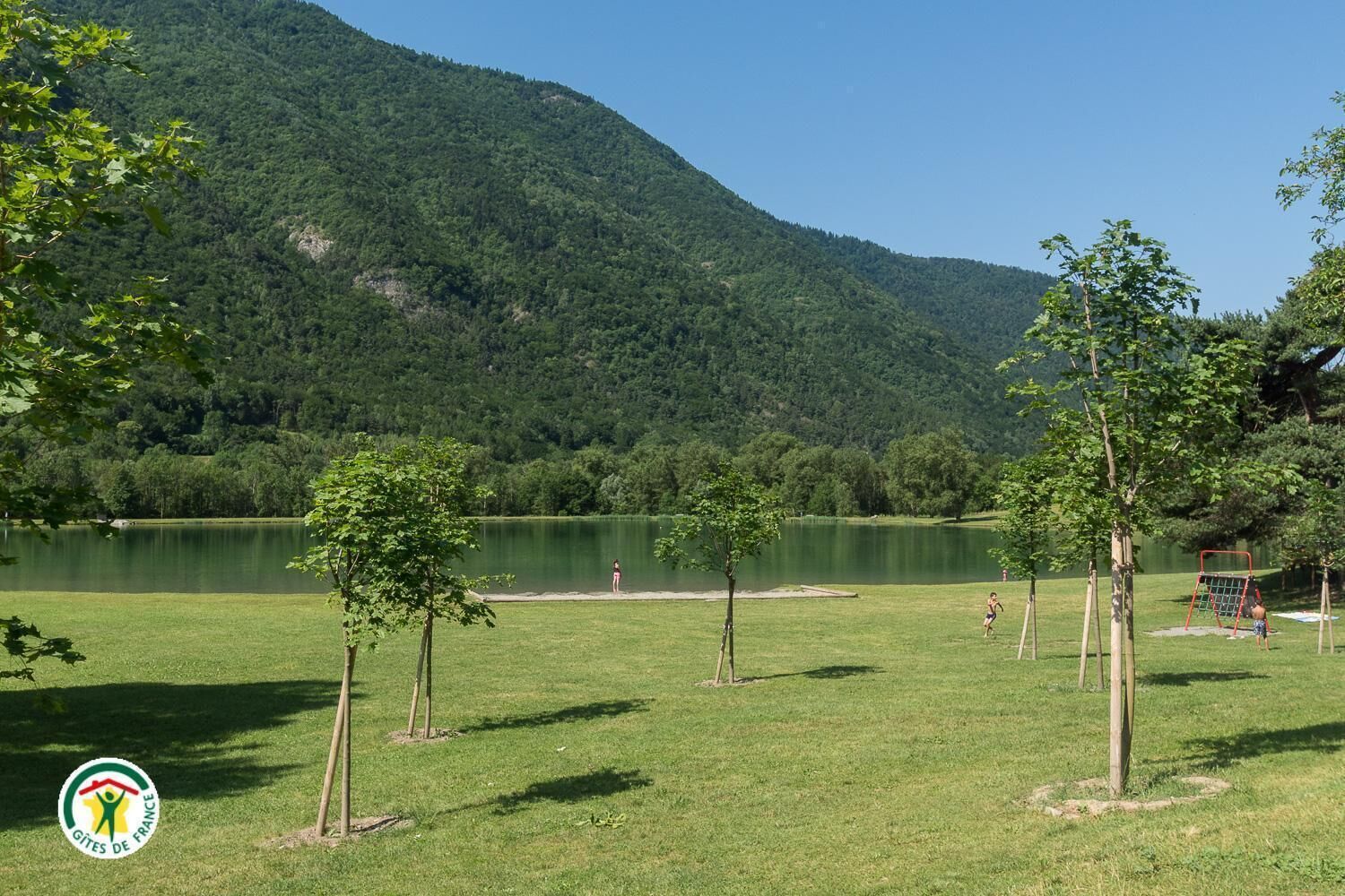 A park with a lake, trees, and a hill in the background.