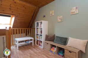 A cozy room with a sloped ceiling, a white bench, a bookshelf, a cushioned bench, and a wall with travel posters. - L'Etoile du Colombier (VALBONNAIS)