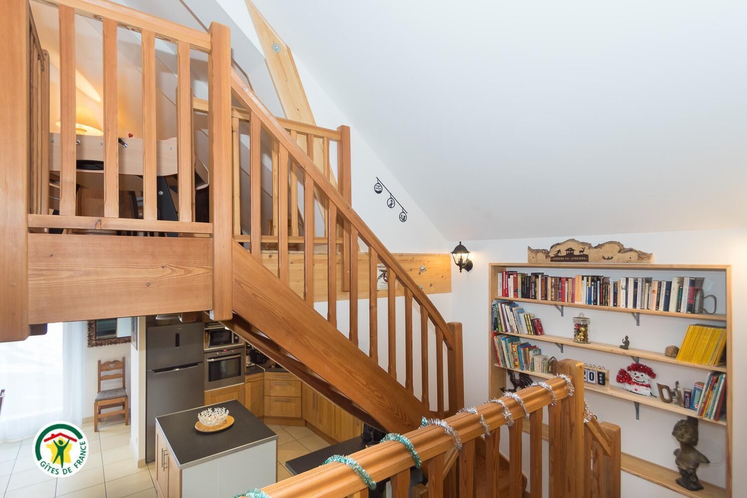 Eine Holztreppe führt zu einer oberen Ebene mit einer Küche und einem Bücherregal.