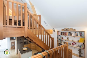 Una escalera de madera que lleva a un nivel superior con una cocina y una estantería.