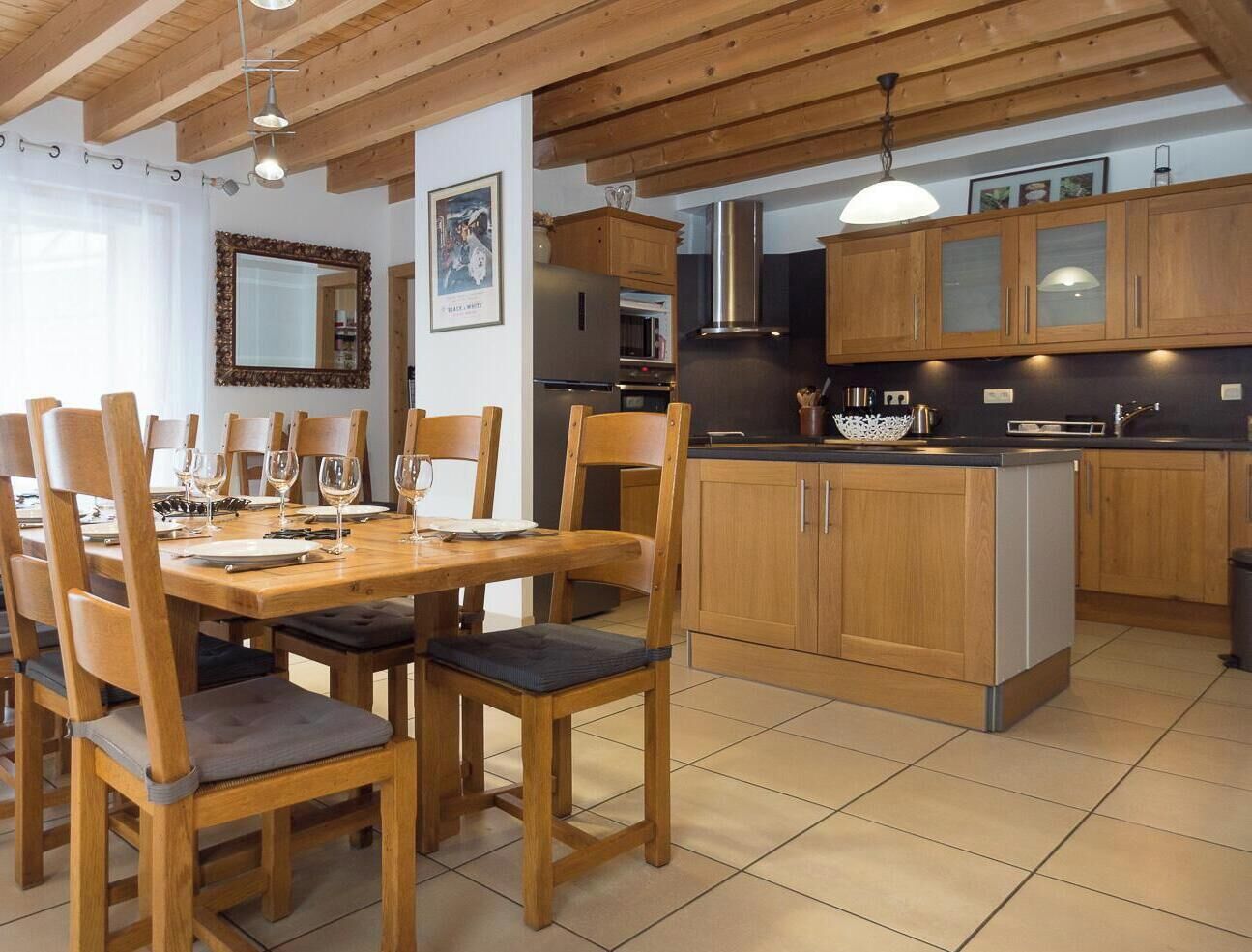 Ein Essbereich mit Holztisch und -stühlen, eine Küche mit Holzschränken und modernen Geräten, sowie ein großes Fenster mit Vorhängen.