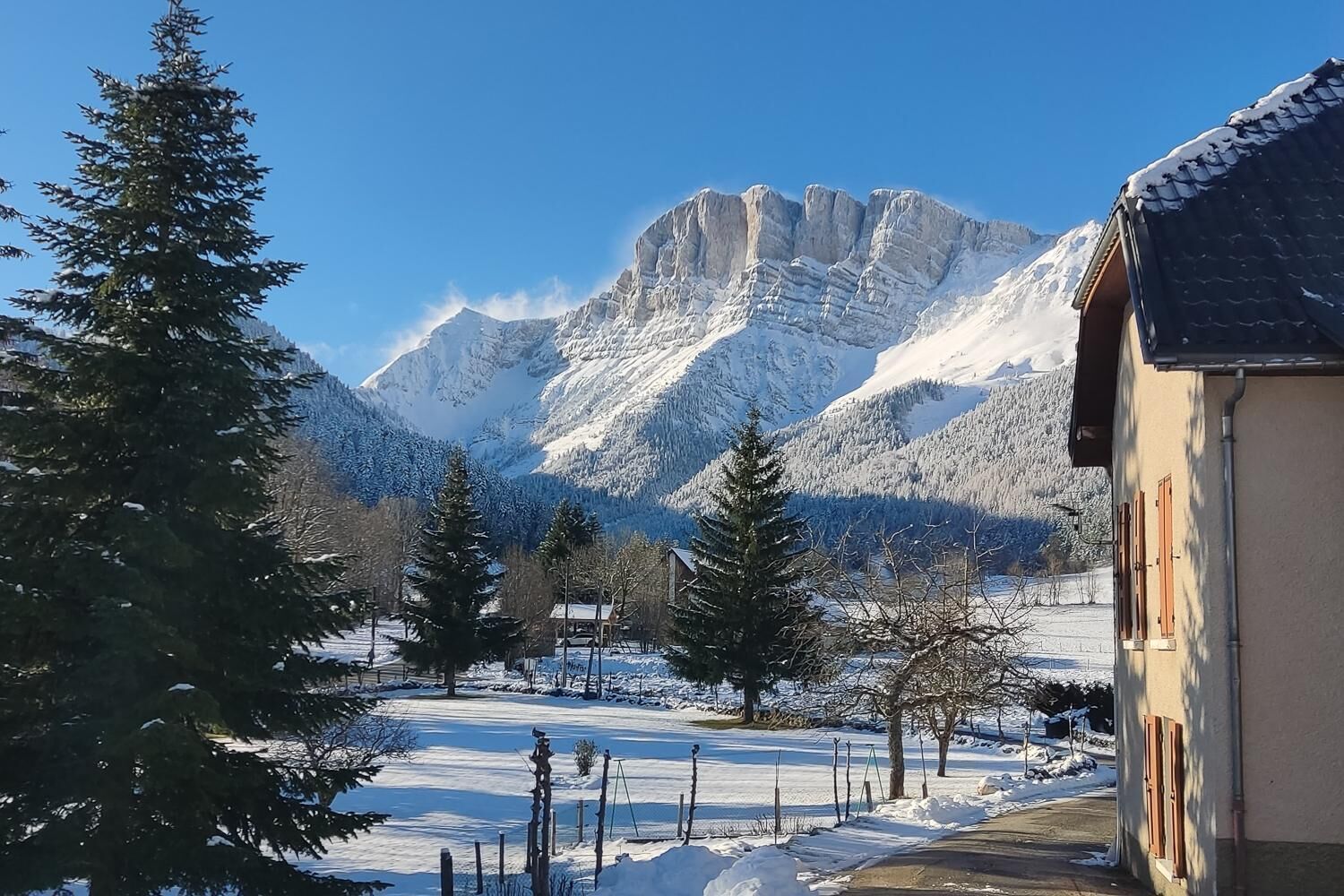 Schneebedeckte Landschaft mit einem Berg im Hintergrund, ein Gebäude mit Satteldach und einem klaren Himmel.
