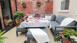An outdoor patio with a table set for a meal, a sofa, and potted plants. - Acorn Cottage (Yarm)
