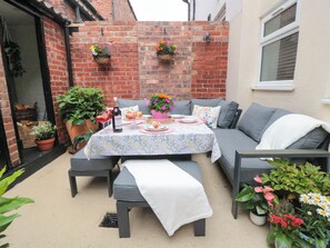 An outdoor patio with a table set for a meal, a sofa, and potted plants. - Acorn Cottage (Yarm)