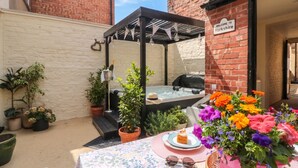 A patio area with a table set for tea, a hot tub, and potted plants. - Acorn Cottage (Yarm)