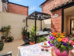 A patio area with a table set for tea, a hot tub, and potted plants. - Acorn Cottage (Yarm)