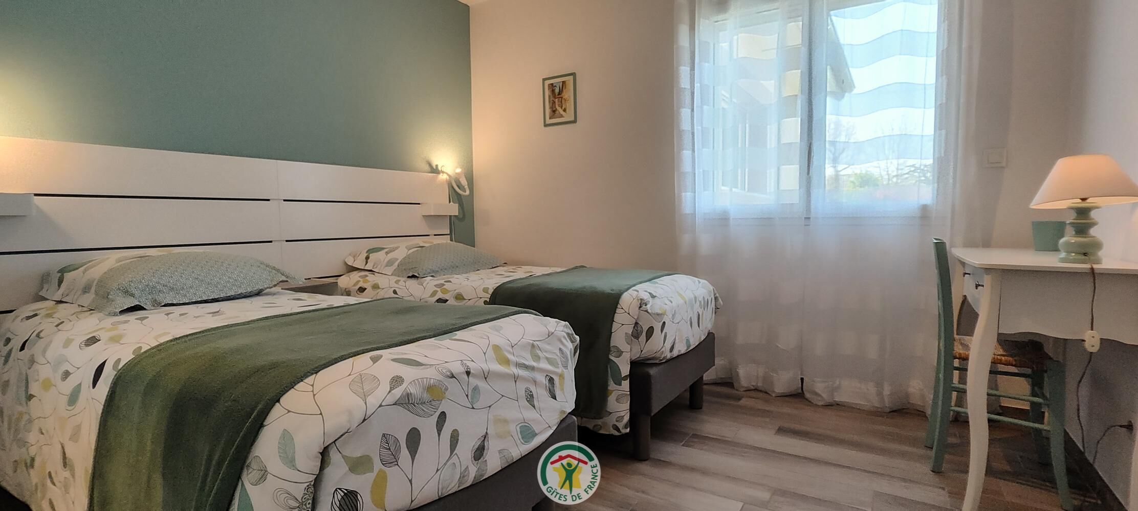 A bedroom with two beds, a desk, and a window with curtains.