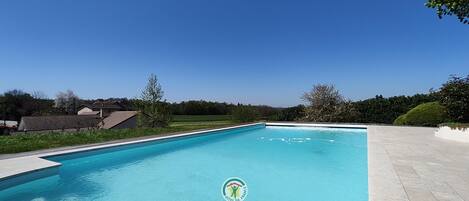 Una piscina rectangular con superficie de agua azul cristalina, rodeada por una solana pavimentada.