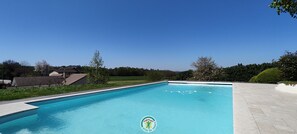 Piscina retangular com superfície de água azul cristalina, rodeada por um deck pavimentado.