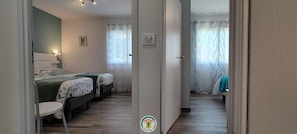 Een slaapkamer met twee bedden, een stoel en een deur naar een andere kamer.