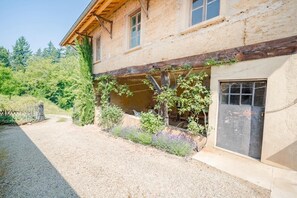 A rustic building with a wooden facade, a gravel driveway, and a garden area with various plants. - Les Jacines - SUCCIEU (SUCCIEU)