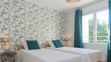 A room with two beds, a window with curtains, and a wall with a floral pattern.