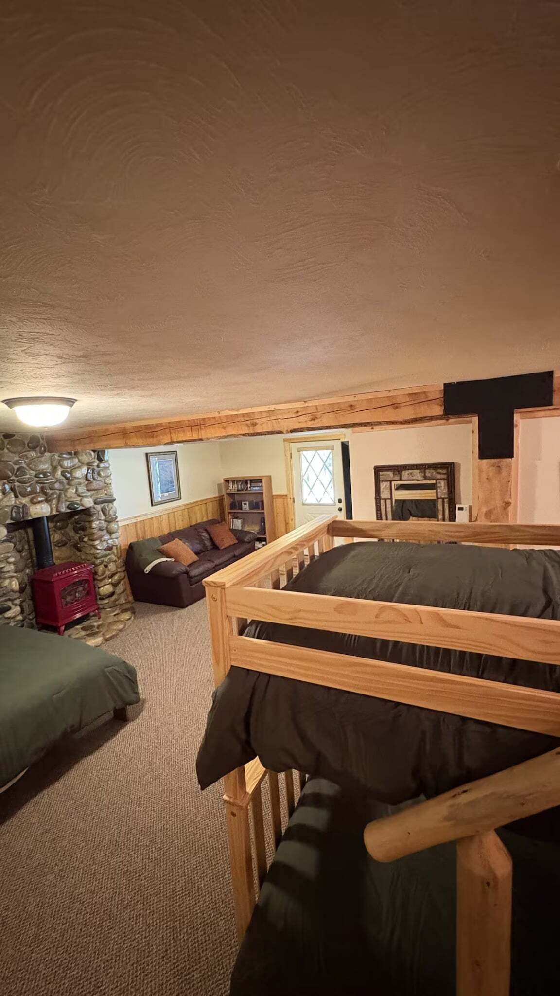 A cozy room with a stone fireplace, a wooden bunk bed, a leather sofa, and a bookshelf.