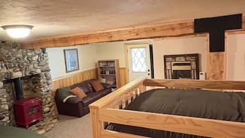 A cozy room with a stone fireplace, a wooden bunk bed, a leather sofa, and a bookshelf.