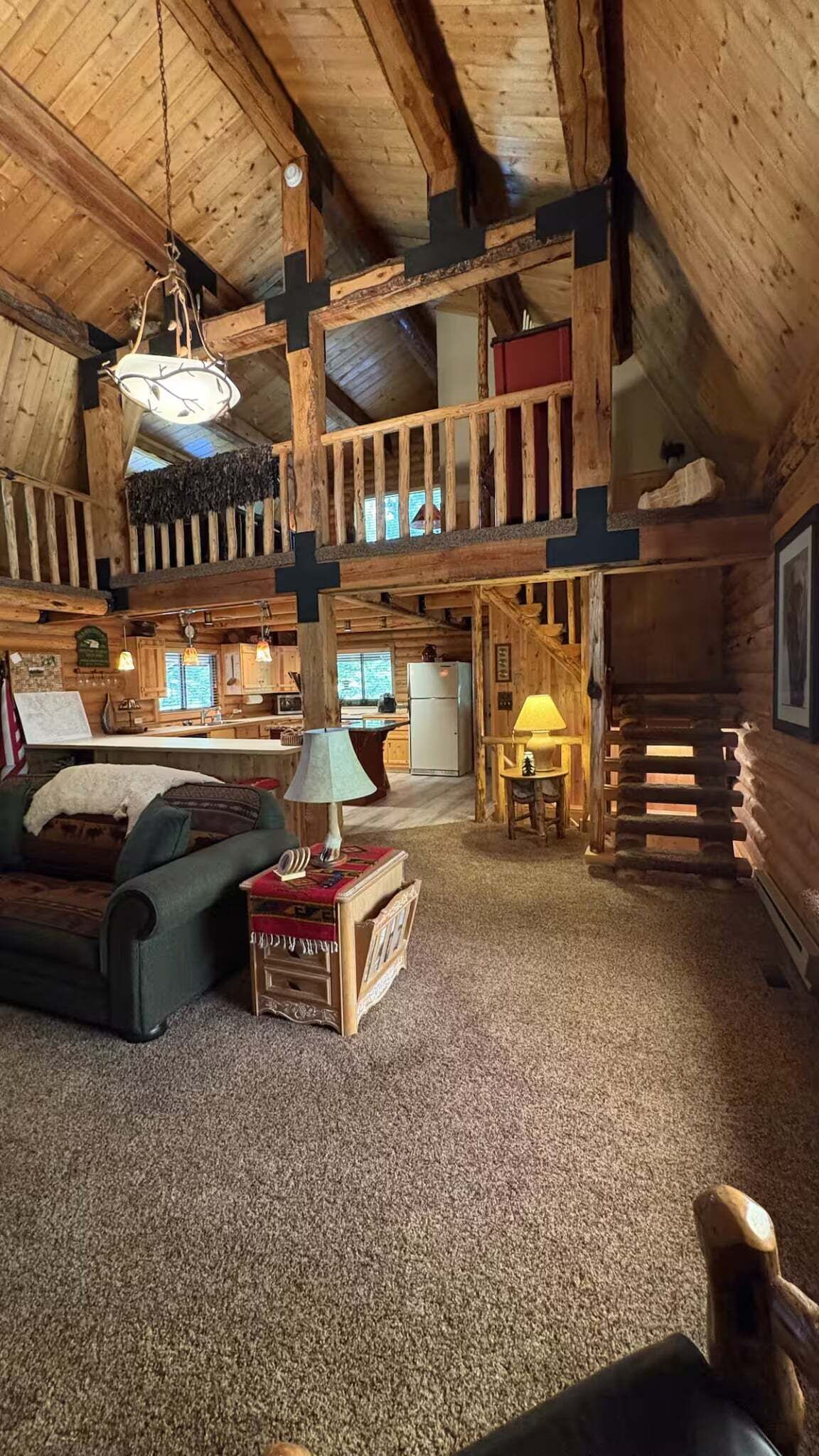 A log cabin interior with a loft bedroom, a dining area, and a kitchen.