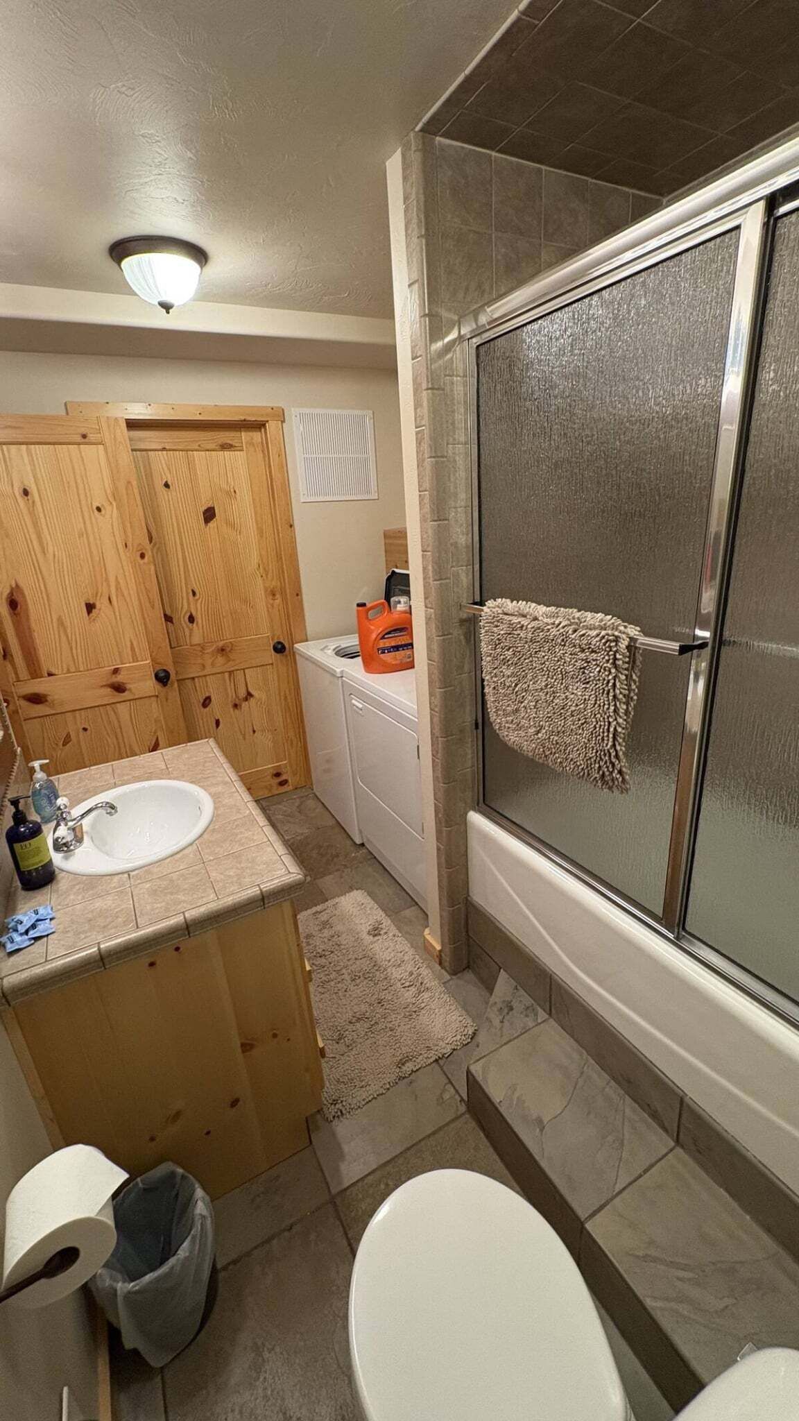 A bathroom with a shower, toilet, sink, and wooden cabinets.
