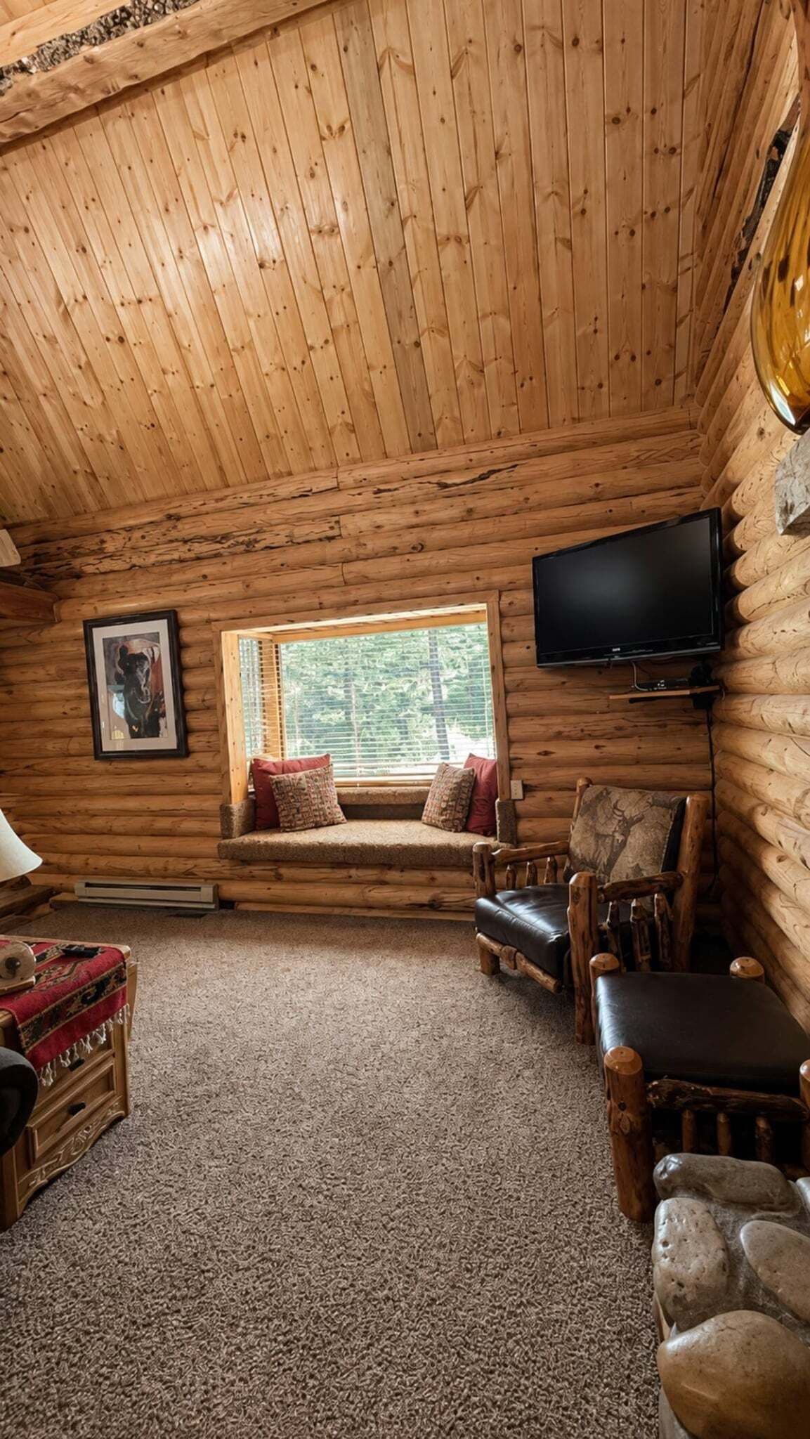 L’intérieur d’une cabane en rondins, avec une télévision, un coin lecture près d’une fenêtre et une cheminée.