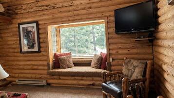 L’intérieur d’une cabane en rondins, avec une télévision, un coin lecture près d’une fenêtre et une cheminée.