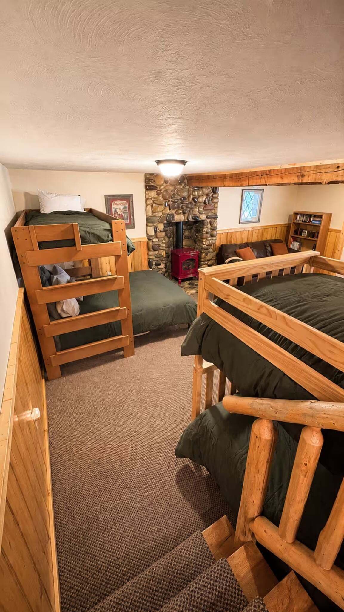 A compact room with bunk beds, a stone fireplace, and a bookshelf.