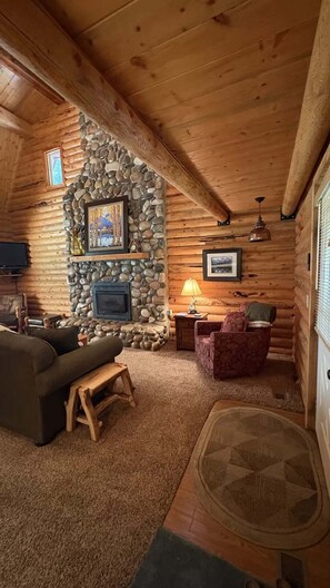 A cozy log cabin interior with a stone fireplace, a sofa, a chair, and a lamp. - Sagebrush Meadows+Hotub+WiFi+20minsYellowstone (Island Park)