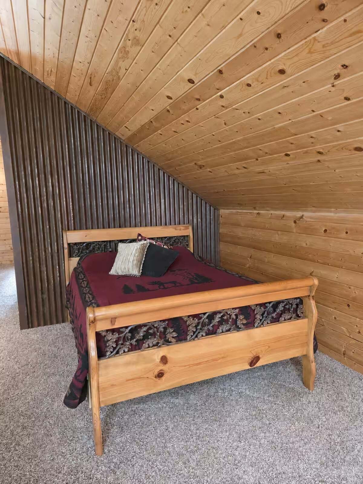 A bedroom with a sloped ceiling, a wooden bed frame, and a patterned bedspread.