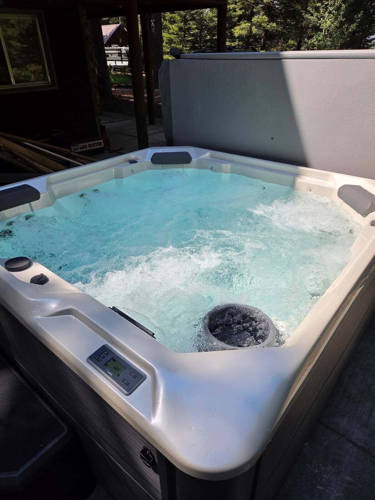 A hot tub with a control panel, surrounded by a wooden deck and trees.