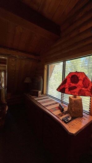 L’intérieur d’une cabane en bois, avec un bureau, une lampe et une fenêtre équipée de stores.