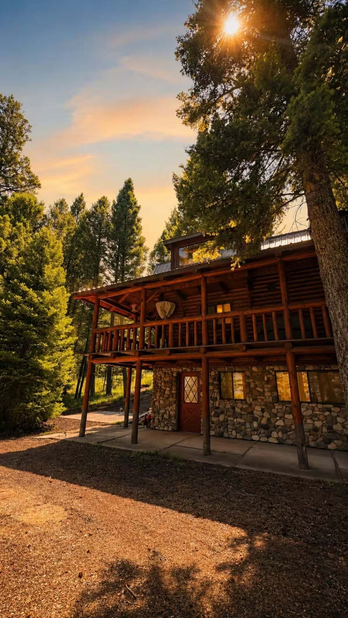 A wooden cabin with a stone foundation, surrounded by trees and a clear sky.